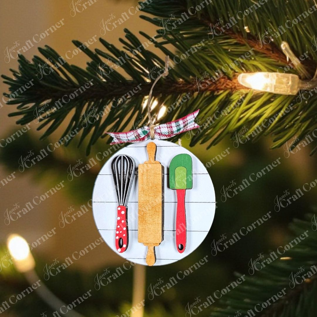 Introducing the Baking Spirits Bright Ornaments by Janet's Craft Corner! This individually painted festive ornament showcases wooden baking utensils, including a whisk, rolling pin, and spatula, each embellished with vibrant accents. Perfectly paired against a rustic backdrop enhanced by green foliage and pinecones, it is elegantly tied together with a plaid ribbon to brighten your holiday season.