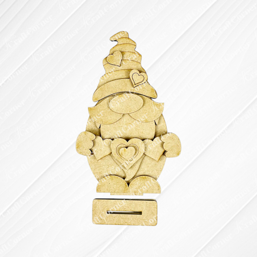 The Valentine Gnome Shelf Sitter from Janet's Craft Corner is a charming home décor piece crafted from light wood. It features a central heart-shaped design and a tall hat with heart details, ideal as is or as part of the DIY seasonal craft kit.