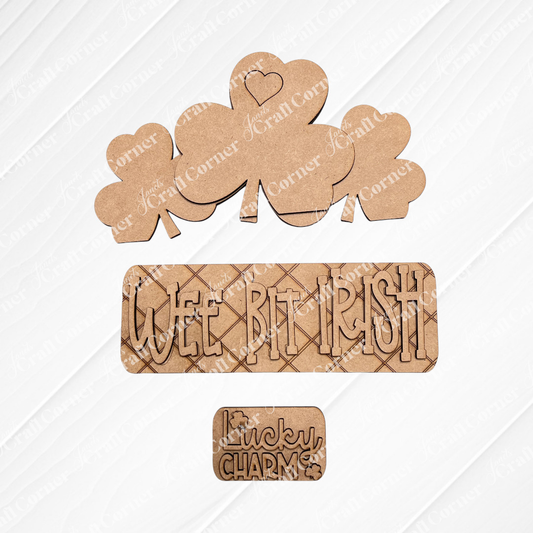 Janet's Craft Corner presents the "Wee Bit Irish" Interchangeable Insert: featuring wooden shamrocks, one with a heart, a plaque reading "WEE BIT IRISH," and a small piece reading "Lucky Charm" beside a shamrock. The burlap background enhances this charming DIY home decor kit.