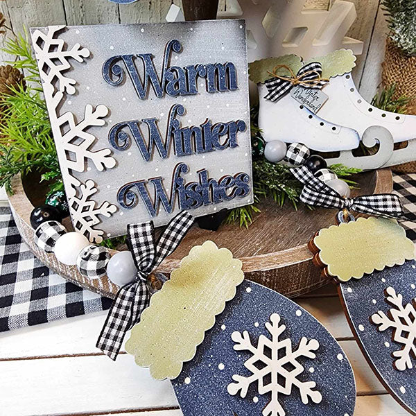 The Winter Wonderland Tiered Tray Set from Janet's Craft Corner is a charming home décor piece that includes "Warm Winter Wishes," snowflake details, skates, and mitten ornaments. Embellished with checkered ribbons and beads on a wooden tray covered with plaid cloth, it's an ideal DIY kit to capture the season's essence.