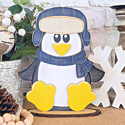 Add a touch of charm to your woodland friends-themed décor with Janet's Craft Corner's Woodland Friends Penguin Shelf Sitter. This adorable penguin, adorned with a scarf and hat, features yellow feet and beak as it sits on a wooden base. Surround it with pinecones, a large wooden snowflake, greenery, and white decorative berries for the perfect display.