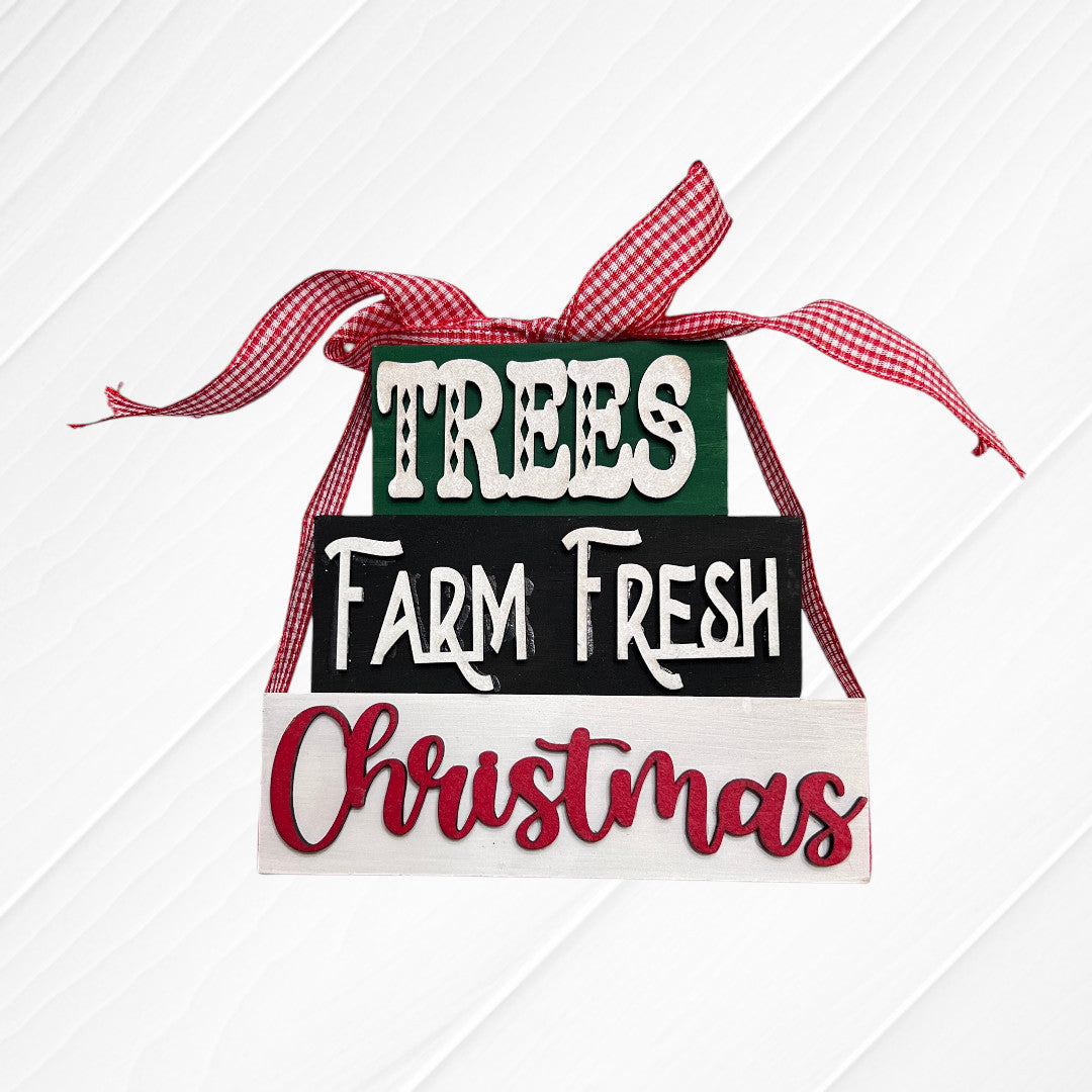 Janet's Craft Corner Word Stacks - Painted: three stacked blocks reading "TREES," "Farm Fresh," and "Christmas," tied with a red and white checked ribbon, displayed on a white wooden background.