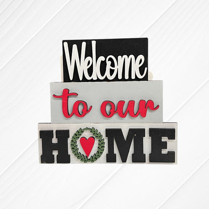 Janet's Craft Corner's Word Stacks - Painted features three stacked white wood blocks reading "Welcome," "to our," and "HOME," with a green wreath and red heart as the "O.