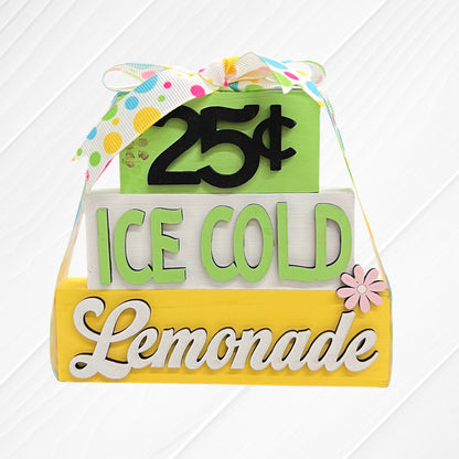 Janet's Craft Corner Word Stacks - Painted: A decorative sign with three stacked blocks, reading "25¢" (green), "ICE COLD" (white), and "Lemonade" (yellow), topped with a colorful ribbon and accented by a small pink flower.