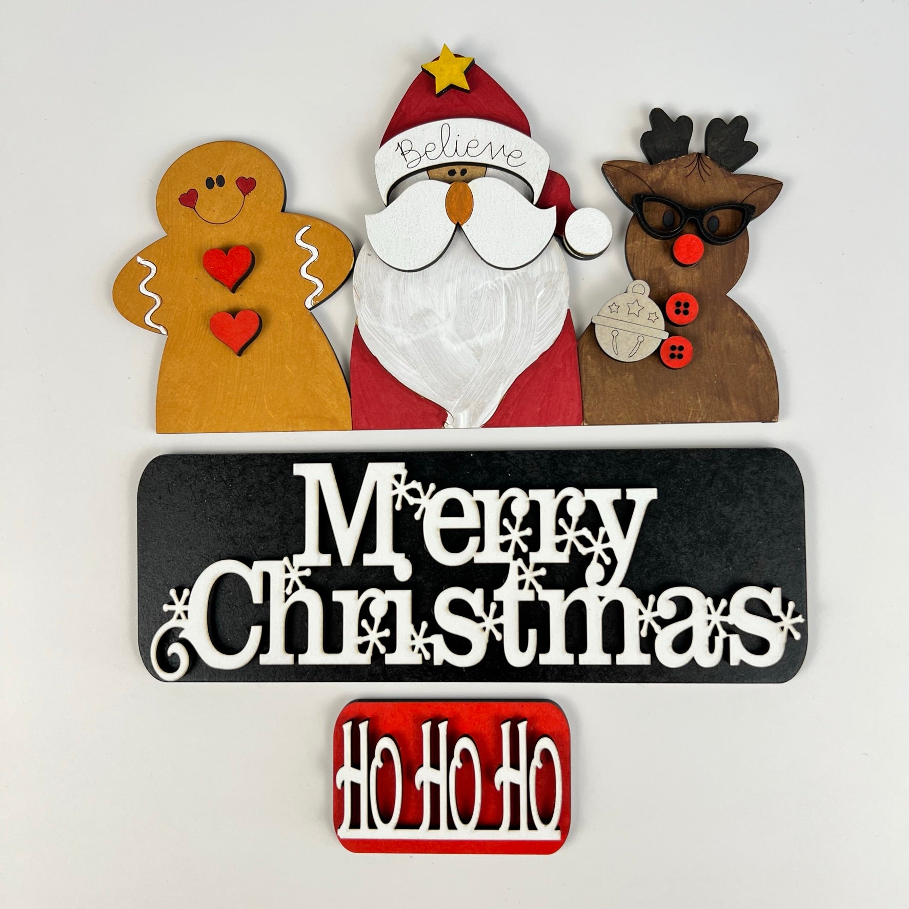 Discover the Merry Christmas Interchangeable Insert from Janet's Craft Corner, a DIY home decor kit featuring hand-painted wooden Christmas decorations such as a gingerbread person, a "Believe" Santa hat, and a reindeer in sunglasses. With interchangeable signs reading "Merry Christmas" and "Ho Ho Ho," it's ideal for those who love festive decor.