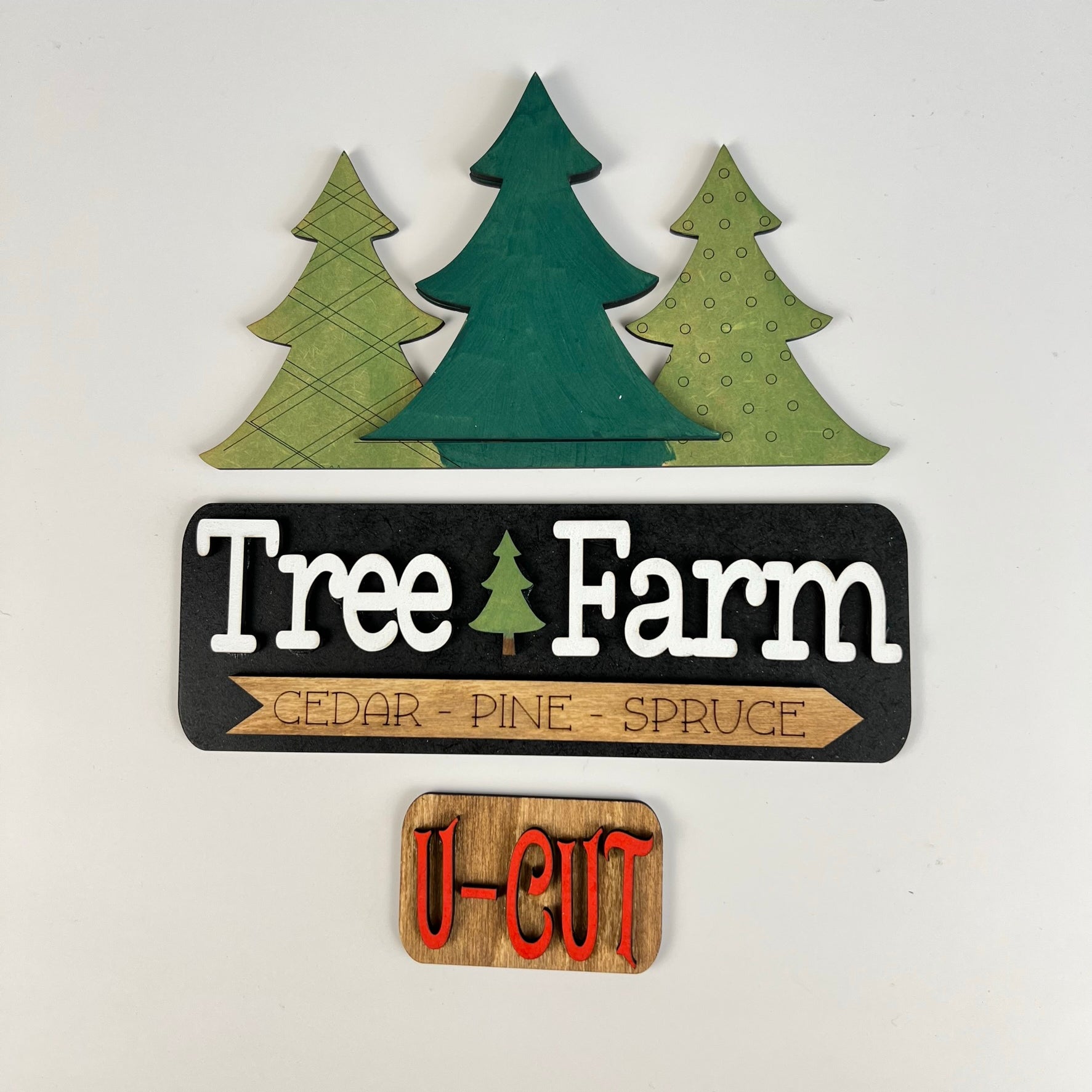 The "Tree Farm Interchangeable Insert" from Janet's Craft Corner is a delightful DIY home decor kit that includes three wooden tree cutouts in different shades of green. The sign displays the words "Cedar - Pine - Spruce," along with a smaller, eye-catching red-lettered sign stating "U-CUT," making it an ideal choice for holiday decorating.