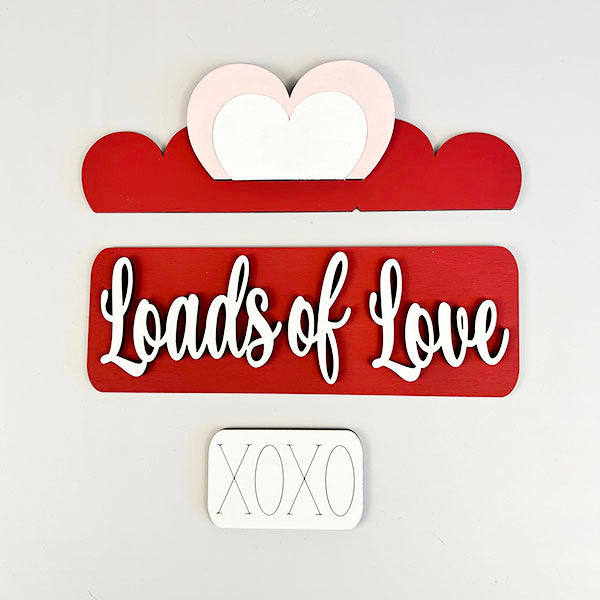 Introducing the Loads of Love Interchangeable Insert by Janet's Craft Corner, this delightful home décor accessory features a striking layered design. It proudly displays a red background adorned with graceful white cursive lettering spelling out "Loads of Love." A charming stylized heart sits above, while bold block letters reading "XOXO" complete the ensemble. Ideal for adding warmth to your living space or incorporating into your own DIY home decor kit.