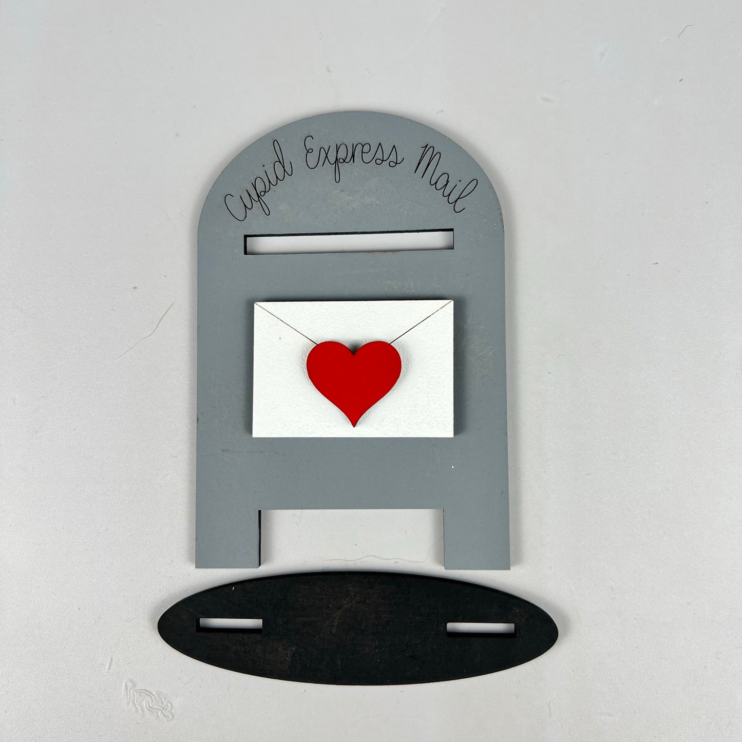 The "Loads of Love Tiered Tray Set" by Janet's Craft Corner includes a charming gray mailbox adorned with "Cupid Express Mail" and a red heart on an envelope. It stands elegantly on a black oval base, adding a whimsical touch of romance to any tiered tray décor.