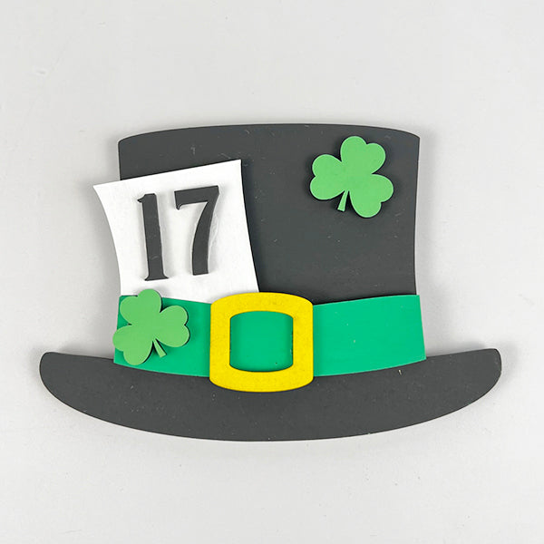 Image of a decorative black top hat featuring a green band and yellow buckle, ideal for festive decorating. Embellished with two green shamrocks and the number "17," it adds a delightful St. Patrick's Day charm to your home décor, making it a perfect component of Janet's Craft Corner's Lucky St Patricks Tiered Tray Kit.