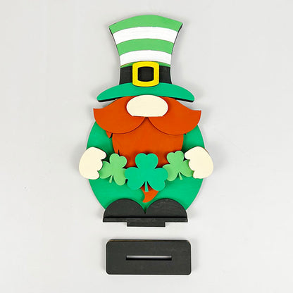 Introducing the Leprechan Gnome Shelf Sitter from Janet's Craft Corner: this striking wooden figure sports a green, white, and black striped hat, an orange beard, and holds green shamrocks. Ideal for home décor enthusiasts, it also includes a rectangular slot beneath for added charm.