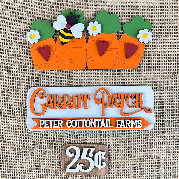 This delightful DIY home decor kit from Janet's Craft Corner, the Carrot Patch Interchangeable Insert, showcases four cartoon carrots adorned with greenery and flowers, accompanied by a bee, a "Carrot Patch Peter Cottontail Farms" plaque, and a quaint rustic sign reading "25¢," all set against a burlap backdrop. It's an ideal choice for enhancing your seasonal displays.