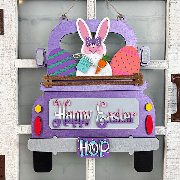 The Easter Bunny Interchangeable Insert from Janet's Craft Corner is a DIY home decor kit that features a charming purple truck adorned with an Easter Bunny sporting a polka dot bow tie and holding a carrot. The truck bed is filled with vibrant Easter eggs and includes a sign that reads "Easter 5¢." The license plate displays "HOP," while the back of the truck sends out cheerful "Happy Easter" wishes.