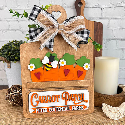 Introducing the Carrot Patch Interchangeable Insert from Janet's Craft Corner. This delightful DIY home decor kit features three painted carrots with heart details and a bee perched on top, labeled "Carrot Patch, Peter Cottontail Farms." Accented with a checked and lace bow, it's the perfect addition to enhance your rustic kitchen setting.