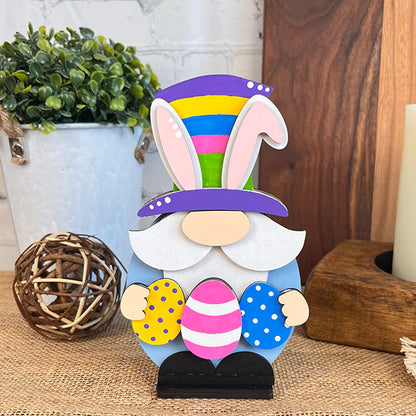 The Easter Egg Gnome from Janet's Craft Corner is an ideal piece for home décor. It features a charming striped top hat with bunny ears and is holding three vibrant eggs. Set on a burlap surface, this figure is complemented by potted plants and various decorative items in the background.