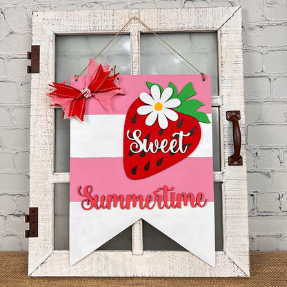 The Strawberry Door Hanger by Janet's Craft Corner features a decorative farmhouse sign on a rustic white window frame, adorned with a large red strawberry, green leaves, and a white flower. The text "Sweet Summertime" appears in red and white against a pink striped background, finished with a red bow.