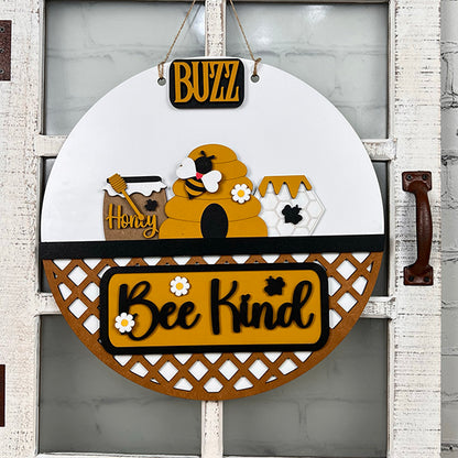 Discover the Bee Interchangeable Insert - Painted from Janet's Craft Corner. This round wooden decorative hanging sign features a charming beehive, bees, and honeycomb motif. It includes the words "Buzz," "Honey," and "Bee Kind" with a lattice pattern at the bottom, offering versatile decor options with its interchangeable bee inserts.